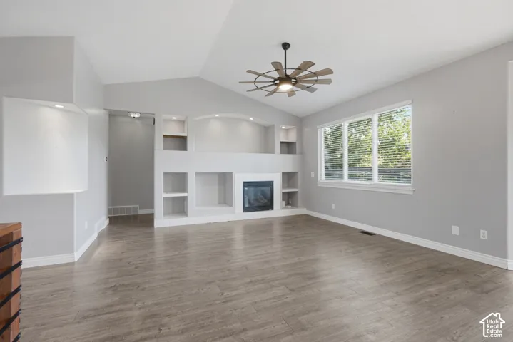 Vaulted ceilings, wood-finish flooring, built-in shelving, an electric fireplace, and a ceiling fan with integrated lighting
