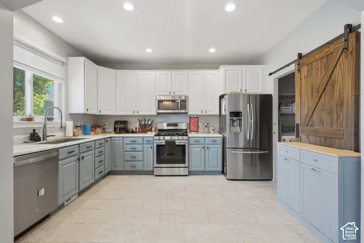 Kitchen featuring white upper cabinetry, blue lower cabinetry, stainless steel appliances, and a wood barn door
