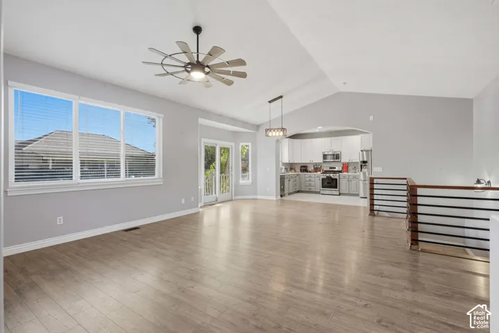 Wood-finish flooring, vaulted ceilings, modern ceiling fan, white trim windows, and an arched kitchen entry