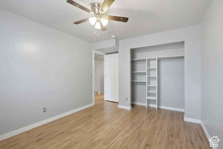 Wood-finish flooring with white trim, recessed closet with shelving and hanging rod, ceiling fan with integrated lighting, and light-colored walls