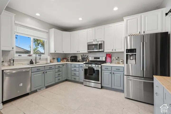 Kitchen featuring stainless steel appliances, upper white cabinetry, lower gray cabinetry, light-toned countertop, and light-toned floor tiling
