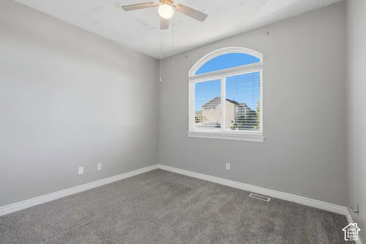 Arched window with blinds, ceiling fan, and carpeted flooring