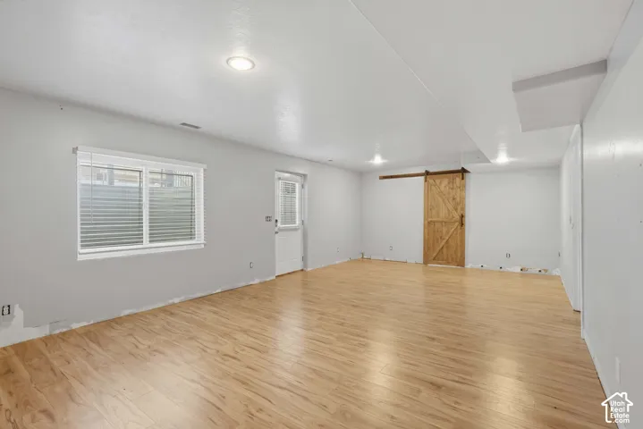 Wood-finish flooring, recessed ceiling lights, white interior door with glass panel, white window blinds, and a wood barn door on a sliding rail