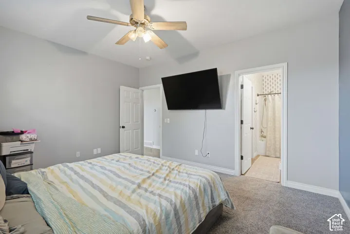 Carpeted room with a ceiling fan, white trim, and a doorway to a bathroom featuring a shower-tub combination