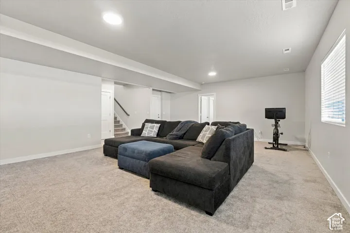 Spacious basement recreation room featuring neutral carpet flooring, recessed ceiling lighting, and abundant natural light from multiple windows