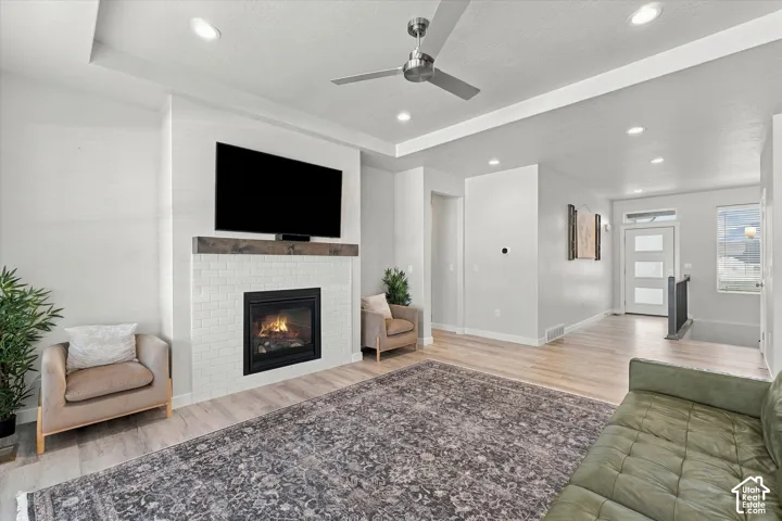 Recessed lighting, wood-finish flooring, ceiling fan, fireplace with tile surround, and tray ceiling
