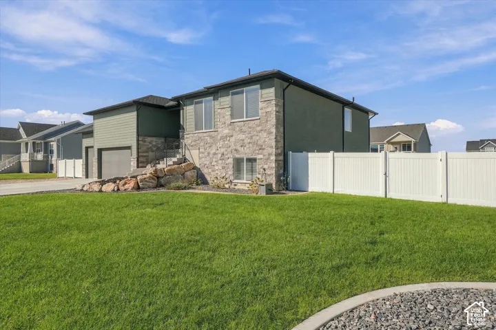 Stone and siding exterior with a two-car garage, front yard landscaping, and white privacy fencing
