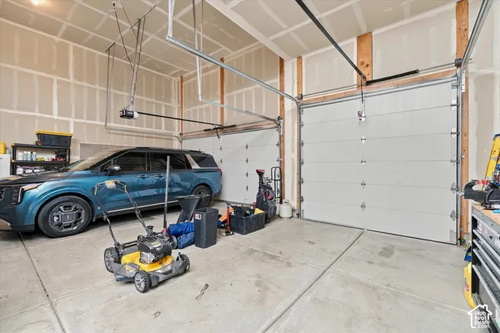 Concrete flooring, exposed wood beam construction, two white garage doors, and overhead garage door openers