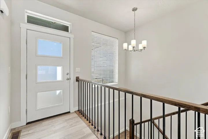 White door with multiple glass inserts, transom window, wood-finish flooring, and a contemporary chandelier