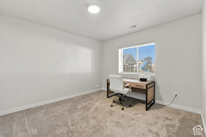 Bright home office featuring neutral wall-to-wall carpeting, recessed ceiling lighting, and expansive windows overlooking the cityscape