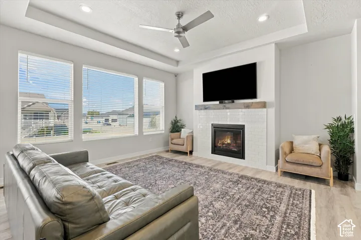 Living area featuring wood-finish flooring, a tray ceiling, recessed lighting, and a white tile fireplace with a wood mantel