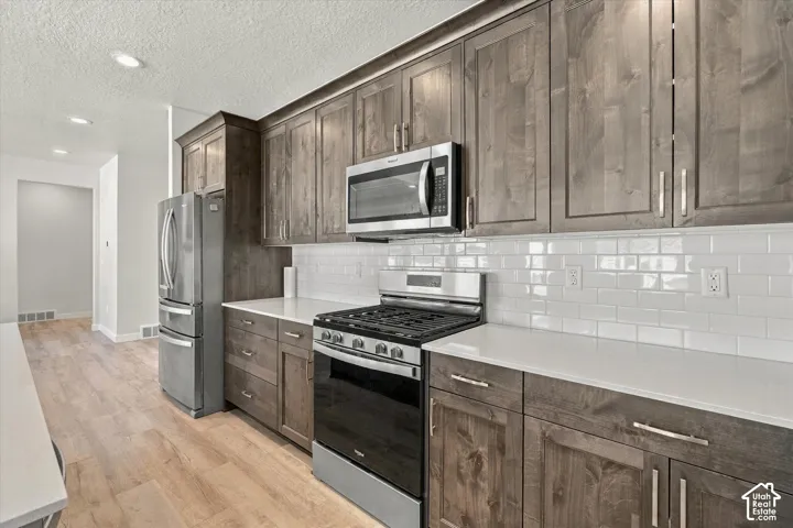 Kitchen featuring wood-finish cabinetry, stainless steel appliances, white subway tile backsplash, and light-toned countertops