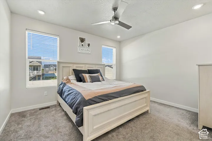 Recessed ceiling lighting, ceiling fan, two windows with blinds, and light-toned carpeting