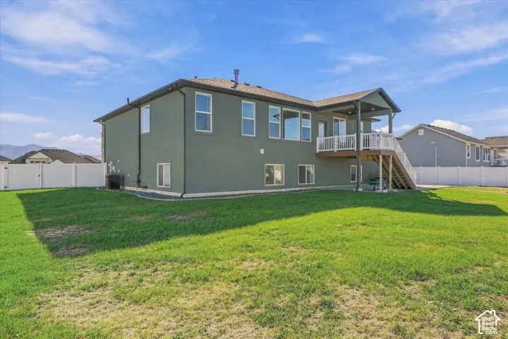 Spacious backyard featuring a covered upper deck with white railings, exterior stairs, and a full fence