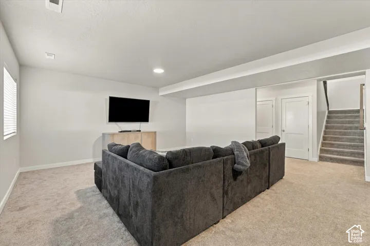 Carpeted living area featuring recessed lighting, a window with blinds, and a staircase with wood-finish handrails