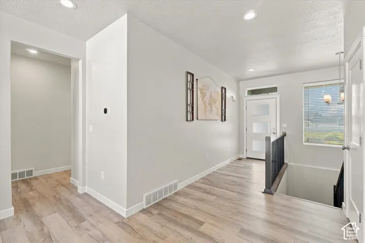 Wood-finish flooring throughout, recessed ceiling lighting, a contemporary front door with frosted glass panels, and a dark metal stair railing