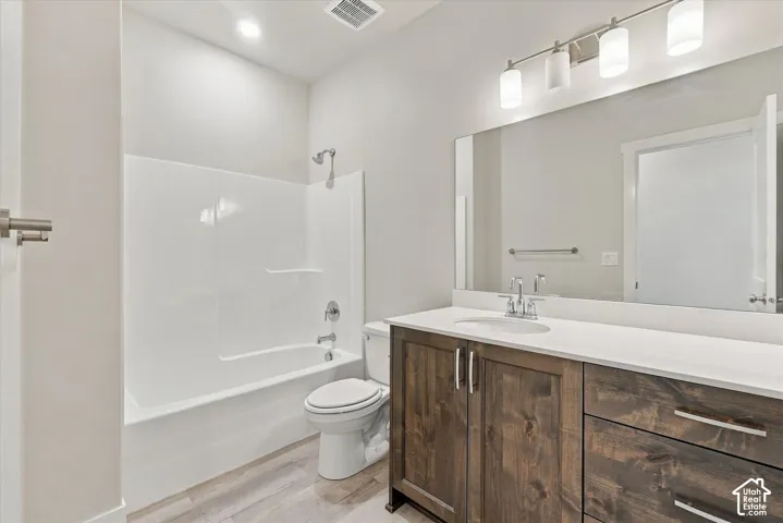 Bathroom featuring a wood-finish vanity with a white countertop, an integrated sink, a large mirror, and a tub-shower combination