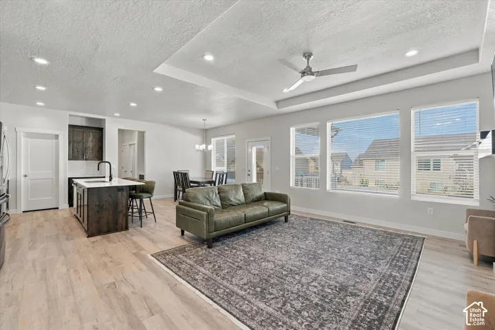 Open-concept living space with light wood-finish flooring, recessed lighting, and a tray ceiling with a ceiling fan