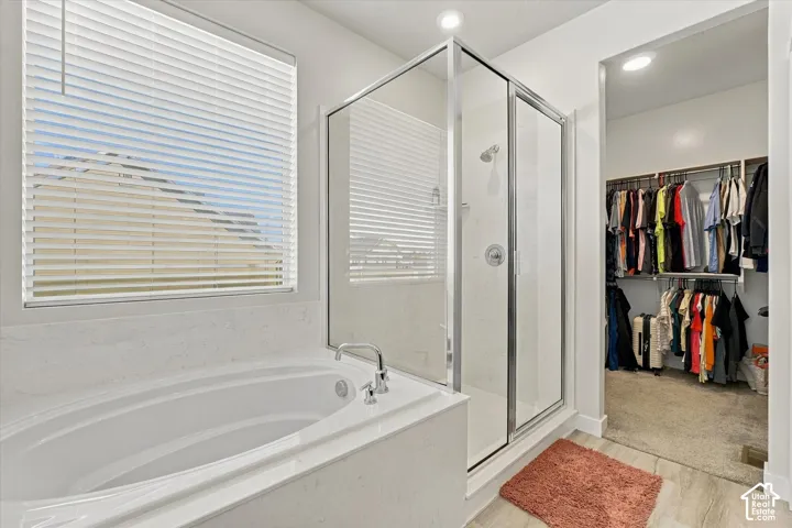 Built-in soaking tub with deck-mounted faucet, glass-enclosed shower, window with blinds, and recessed lighting