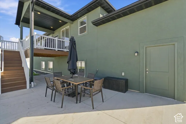 Ground-level concrete patio with an exterior door, a covered deck, and a multi-level staircase with white railings