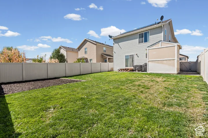 Expansive grassy yard with a privacy fence, a dedicated garden bed, and a rear patio with sliding door access