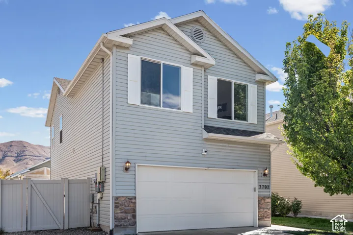 Light-colored siding exterior with a stone veneer accent, two-car garage, and white window shutters