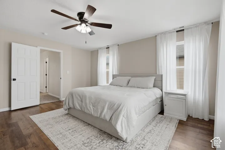 Wood-finish flooring, two large windows, ceiling fan with integrated lighting, and a white paneled door