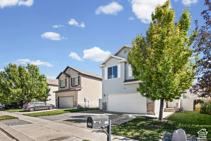 Two-story residential architecture with siding and stone accents, featuring an attached garage, a paved driveway, and established landscaping