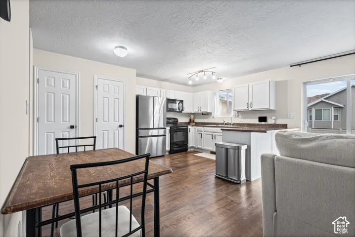 Spacious kitchen featuring white cabinetry, dark countertops, stainless steel appliances, and wood-finish flooring