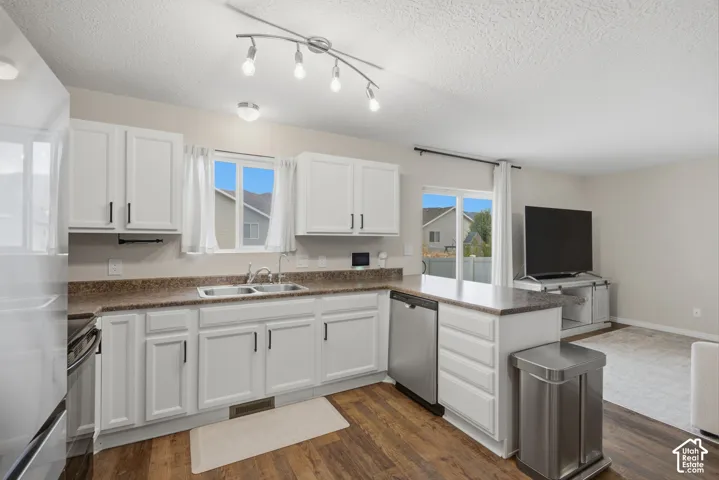 White cabinetry with black hardware, wood-finish flooring, stainless steel dishwasher, double basin sink, and a sliding glass door