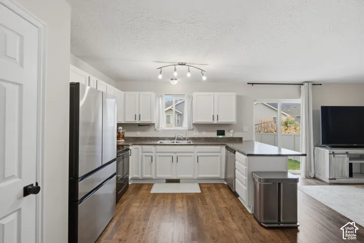 White cabinetry, granite-style countertops, stainless steel appliances, wood-finish flooring, and a sliding glass door