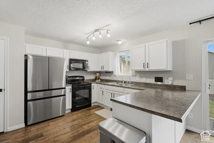 Kitchen featuring wood-finish flooring, white cabinetry with dark hardware, stainless steel appliances, a U-shaped countertop, and a track lighting fixture