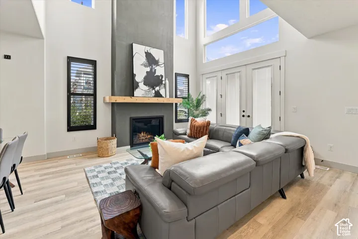 Soaring great room features a gas fireplace with wood mantel, floor-to-ceiling windows with skylights flooding the space with natural light, and gleaming wood-finish flooring throughout
