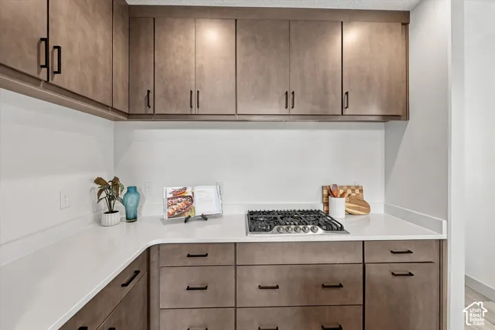 White countertops, rich wood-finish cabinetry, under-cabinet lighting, and a built-in gas range