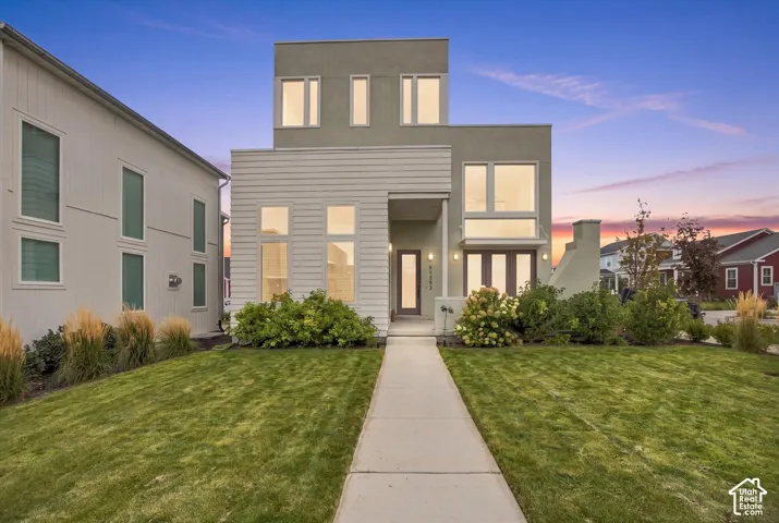 Contemporary exterior featuring multiple window styles, a concrete pathway, manicured lawn, and established shrubbery