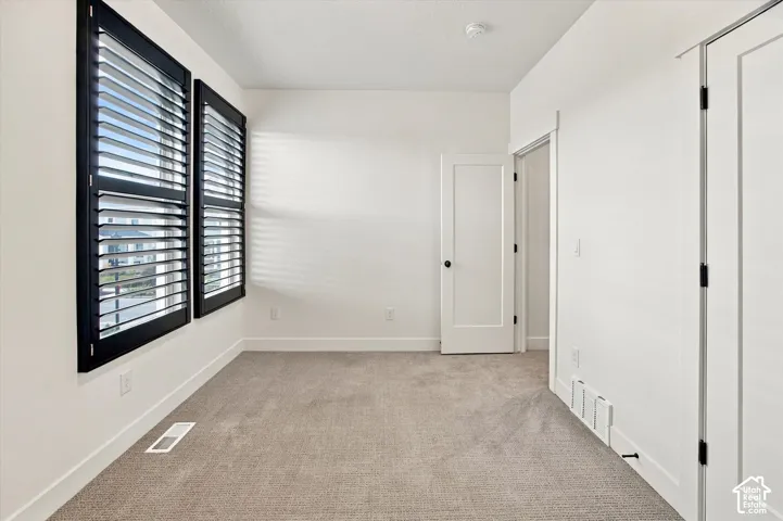 Bright, neutral bedroom offering carpet flooring, black plantation shutters with white trim, multiple closet doors, and clean white walls with recessed lighting throughout