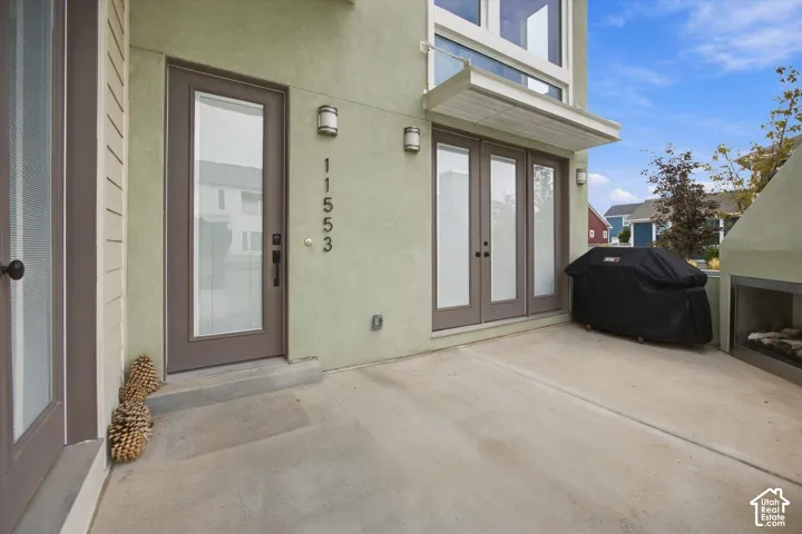 Modern entrance featuring a concrete patio with clean geometric lines, dual frosted-glass entry doors with dark-finish frames, brushed-metal wall sconces, and house numbers mounted on the cream-colored exterior wall