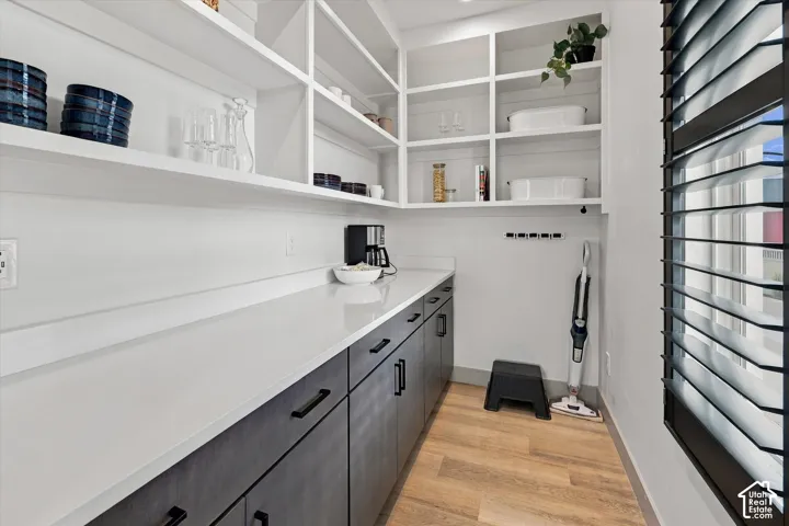 Custom built-in shelving, white countertops, dark wood-finish cabinetry, wood-finish flooring, and a window with plantation shutters
