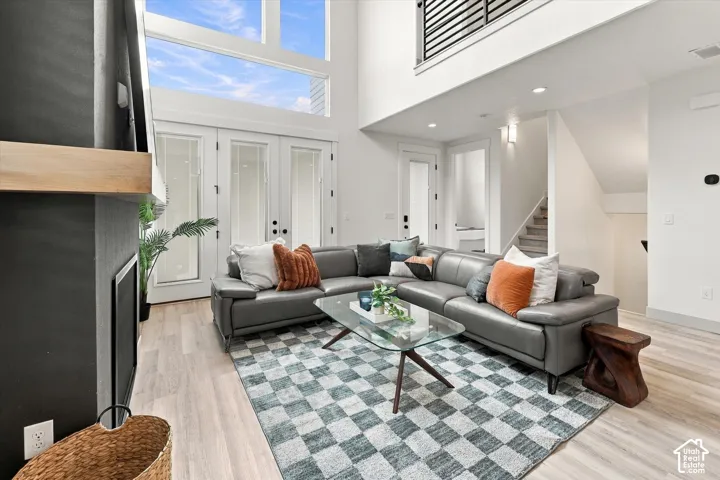 Two-story living area with high ceilings, large windows, light wood-finish flooring, and a contemporary fireplace with a wood mantel