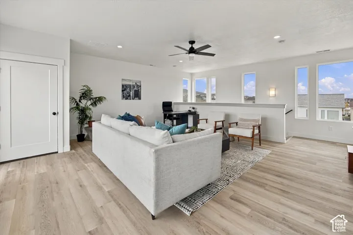 Spacious open-concept room featuring wood-finish flooring, multiple windows, a ceiling fan, and recessed lighting