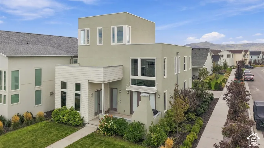 Contemporary stucco exterior with a flat roofline, an integrated covered entry, multiple large windows, and a landscaped front yard