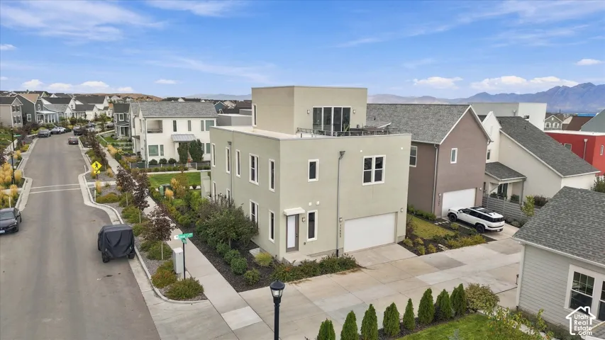 Modern architectural residence featuring a clean-lined cream and tan exterior with multi-pane windows, an attached two-car garage, and manicured front landscaping with evergreen plantings and concrete hardscaping