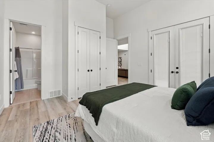 Spacious primary bedroom featuring wood-finish flooring, abundant natural light from multiple windows, and generous closet storage with white bi-fold doors