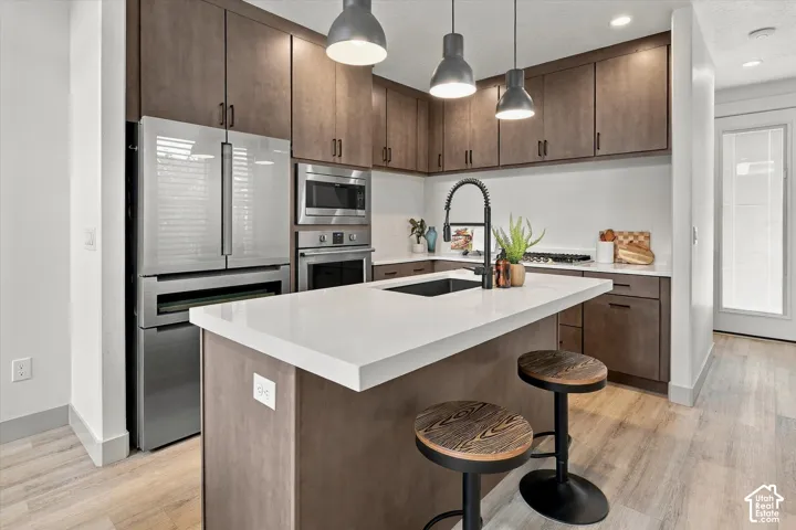 Modern kitchen featuring wood-finish cabinetry, stainless steel appliances, a white solid surface island, and wood-finish flooring