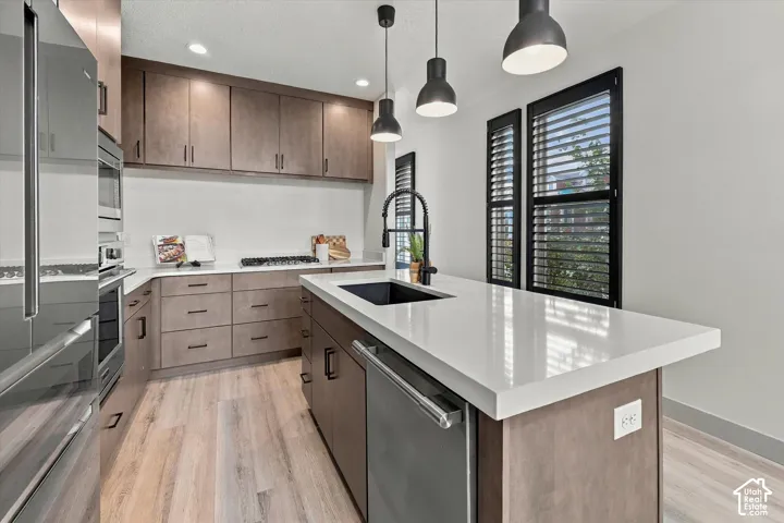 Kitchen featuring wood-finish flooring, stainless steel appliances, white countertops, built-in cabinetry, and pendant lighting