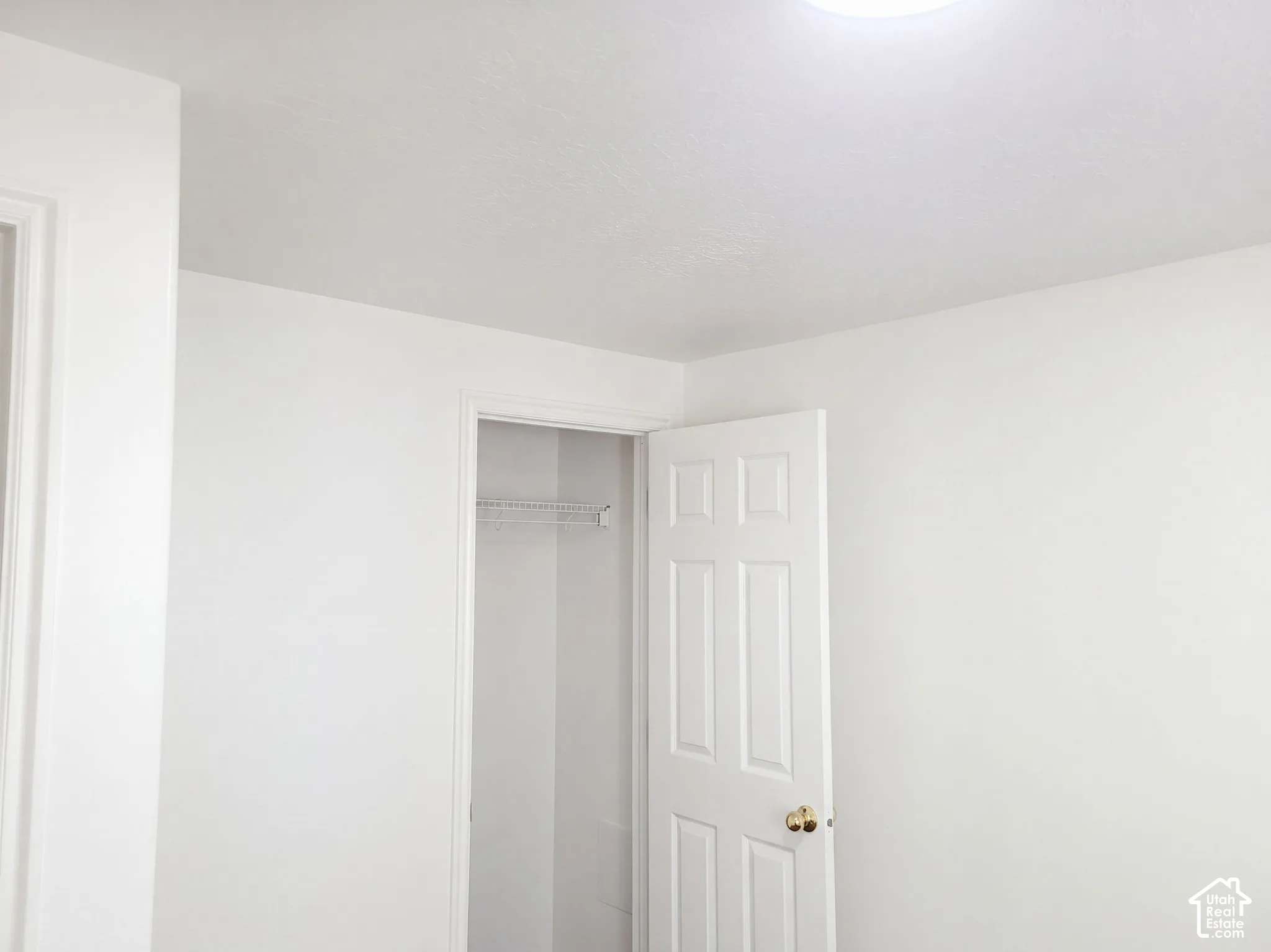 White interior walls with a white ceiling, featuring a flush-mount ceiling light and a white paneled door with a brass-finish knob