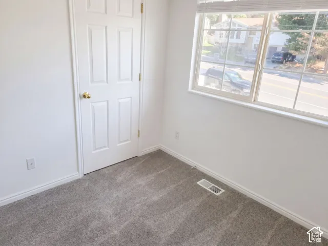 Light gray carpet, white walls, white trim, white paneled door with gold-toned hardware, and a window with white blinds