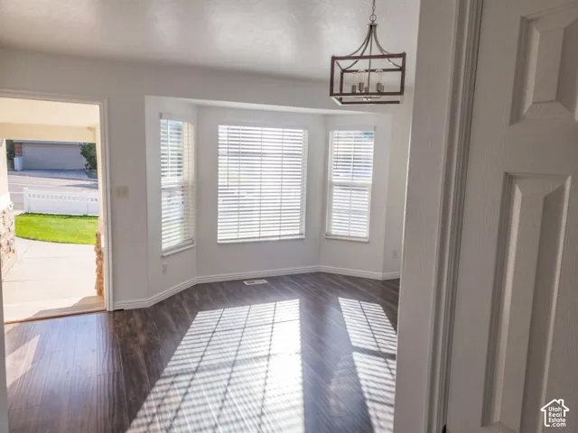 Bay window with white blinds, wood-finish flooring, white baseboards, and a modern chandelier