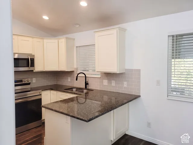 Kitchen featuring perimeter cabinetry, dark stone countertops, stainless steel appliances, a subway tile backsplash, and a double basin sink with a black-finish faucet
