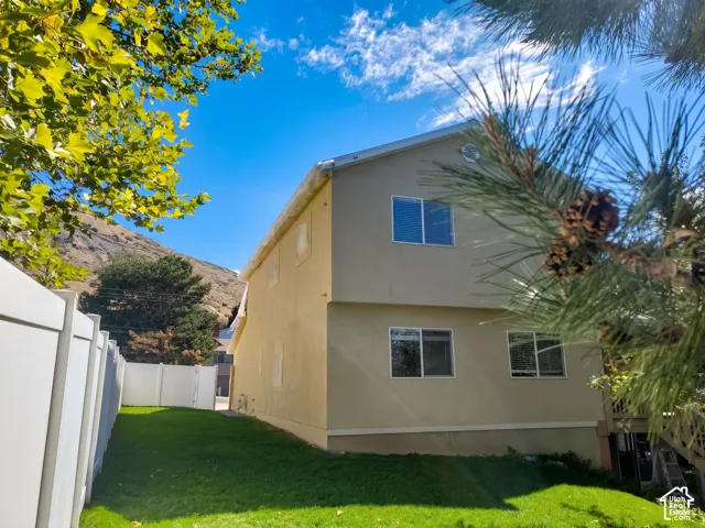 Two-story exterior with a neutral stucco finish, multiple windows, and a full white vinyl fence enclosing a grass lawn